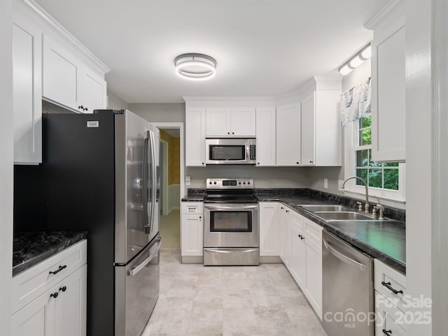 kitchen featuring appliances with stainless steel finishes, a sink, dark countertops, and white cabinetry