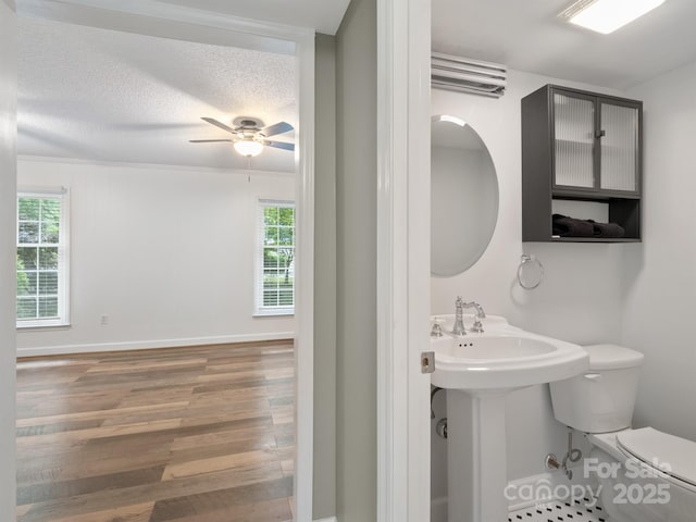 bathroom with toilet, healthy amount of natural light, wood finished floors, and ceiling fan