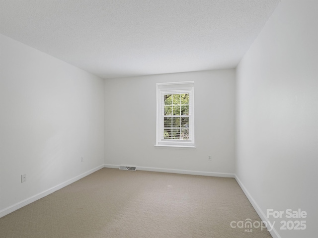 empty room with light colored carpet, baseboards, and a textured ceiling