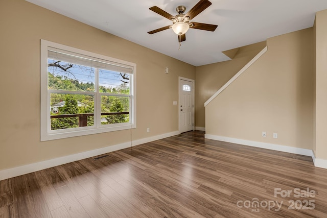 unfurnished living room with ceiling fan, visible vents, wood finished floors, stairway, and baseboards