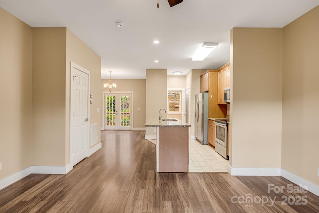 kitchen featuring appliances with stainless steel finishes, baseboards, light stone counters, light wood finished floors, and a chandelier