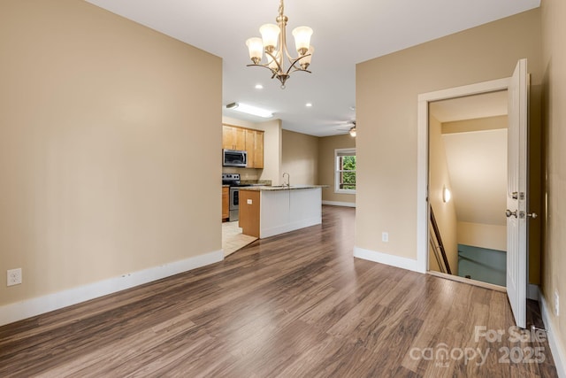 unfurnished living room with wood finished floors, a sink, baseboards, an inviting chandelier, and recessed lighting