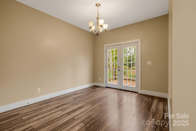 empty room featuring baseboards, dark wood finished floors, a notable chandelier, and french doors