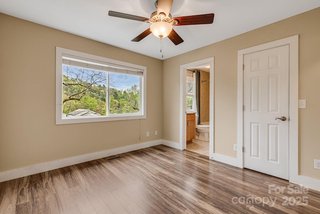 unfurnished bedroom featuring a ceiling fan, visible vents, wood finished floors, baseboards, and ensuite bath