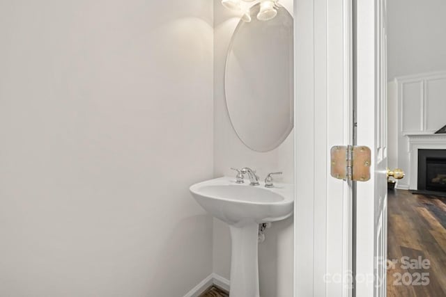 bathroom with a fireplace, wood finished floors, baseboards, and a sink