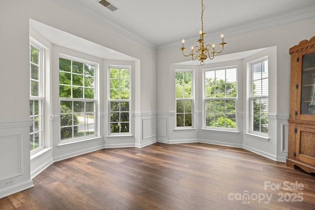 unfurnished dining area featuring an inviting chandelier, a wainscoted wall, visible vents, ornamental molding, and wood finished floors