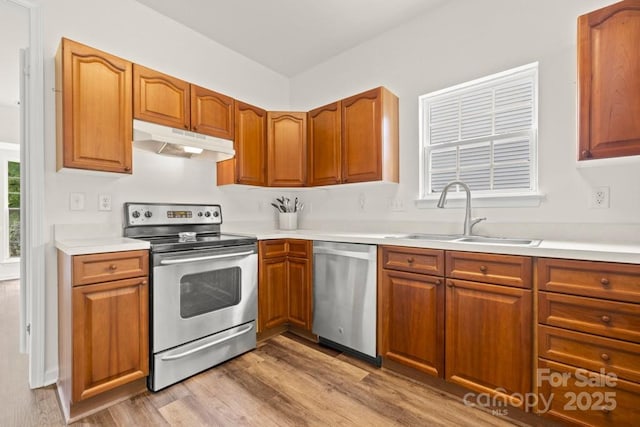 kitchen with a sink, stainless steel appliances, under cabinet range hood, light wood-style flooring, and light countertops