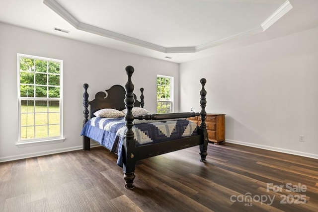 bedroom featuring a tray ceiling, crown molding, visible vents, baseboards, and wood finished floors