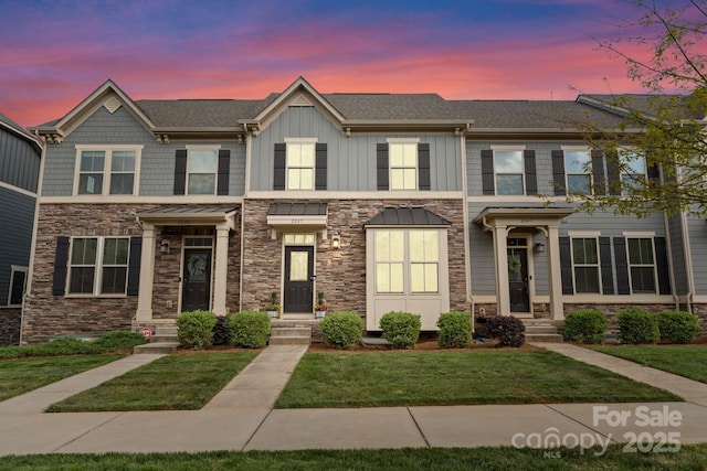 townhome / multi-family property featuring board and batten siding, roof with shingles, stone siding, and a lawn