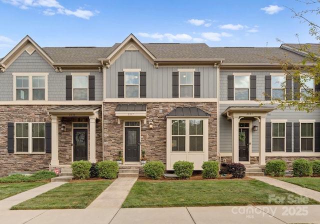 townhome / multi-family property featuring a shingled roof, a front lawn, stone siding, and board and batten siding