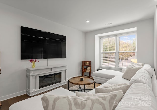 living area with dark wood finished floors, visible vents, baseboards, a glass covered fireplace, and recessed lighting