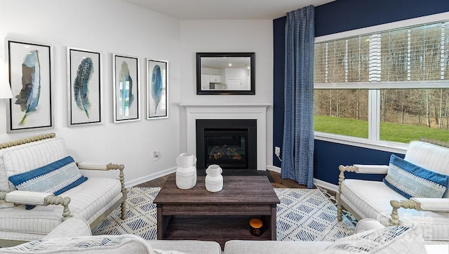living area with baseboards, a glass covered fireplace, and wood finished floors