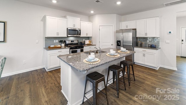 kitchen with visible vents, appliances with stainless steel finishes, a sink, baseboards, and a breakfast bar