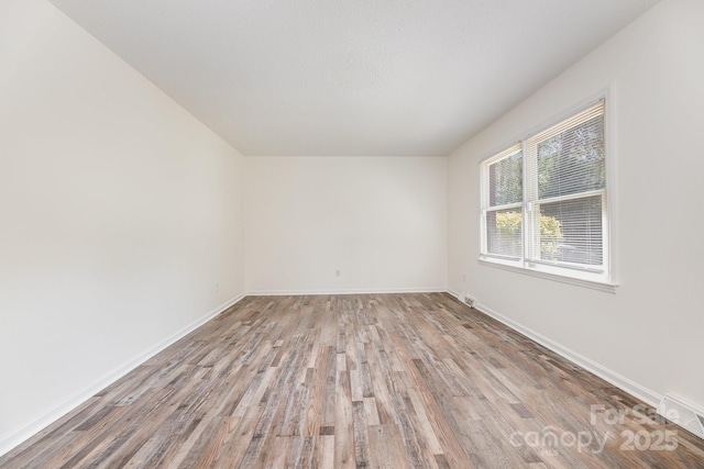 unfurnished room with baseboards, visible vents, and wood finished floors