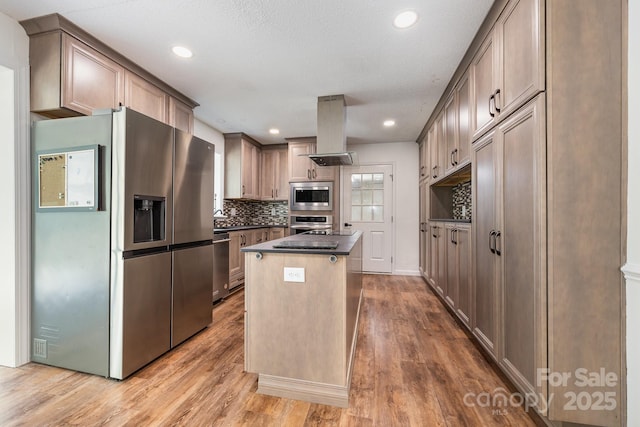 kitchen with light wood finished floors, island exhaust hood, backsplash, dark countertops, and appliances with stainless steel finishes