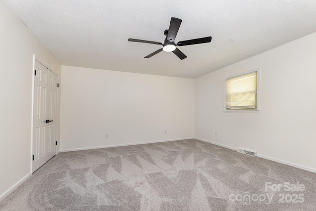 empty room featuring light colored carpet, visible vents, ceiling fan, and baseboards