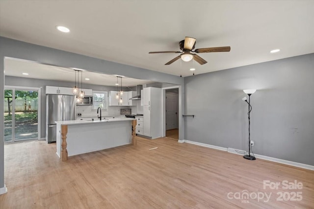 135 Mcshag Dr, Kannapolis, NC 28081 - kitchen featuring light wood-style floors, ceiling fan, wall chimney range hood, white cabinetry, and stainless steel appliances