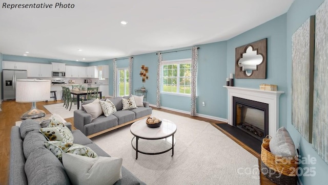 living area with recessed lighting, baseboards, a glass covered fireplace, and light wood-type flooring
