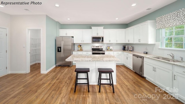 kitchen featuring white cabinets, stainless steel appliances, a kitchen island, and a sink