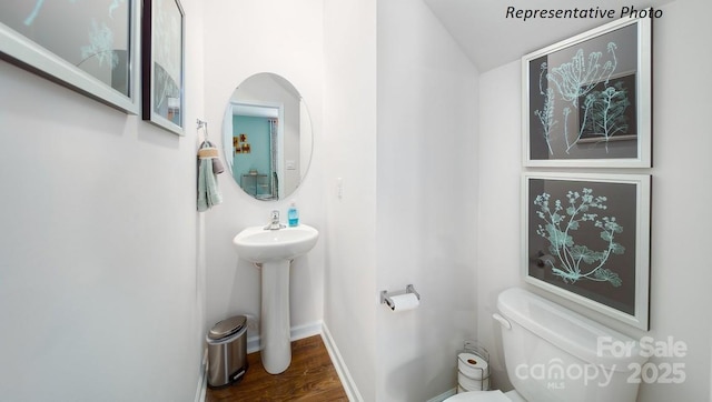 bathroom with wood finished floors, toilet, a sink, baseboards, and lofted ceiling