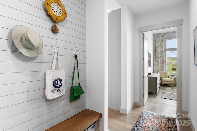 mudroom featuring baseboards, light wood-style flooring, and wooden walls