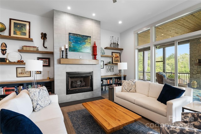 living area with recessed lighting, a tiled fireplace, and wood finished floors