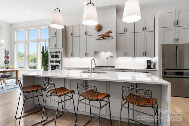kitchen featuring a sink, light countertops, light wood-style flooring, stainless steel appliances, and pendant lighting