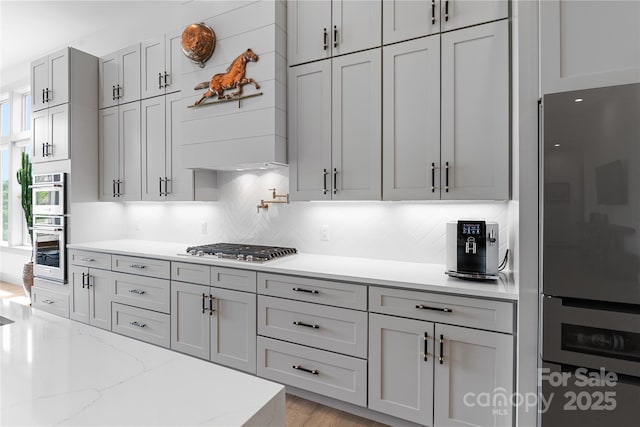 kitchen featuring light stone counters, tasteful backsplash, stainless steel appliances, and light wood finished floors
