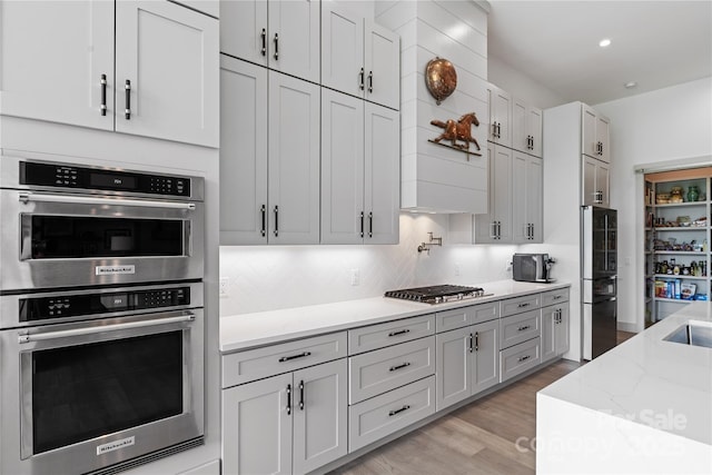 kitchen with decorative backsplash, light stone countertops, light wood-style floors, stainless steel appliances, and recessed lighting