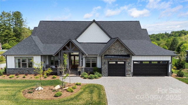 view of front of house with a front lawn, stone siding, a garage, board and batten siding, and decorative driveway