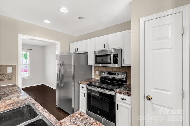 kitchen featuring stainless steel appliances, visible vents, dark wood-style flooring, white cabinetry, and backsplash