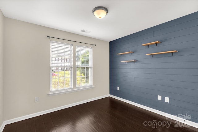 spare room with dark wood finished floors, visible vents, baseboards, and wooden walls