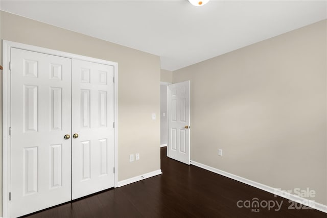 unfurnished bedroom featuring a closet, dark wood-style flooring, and baseboards