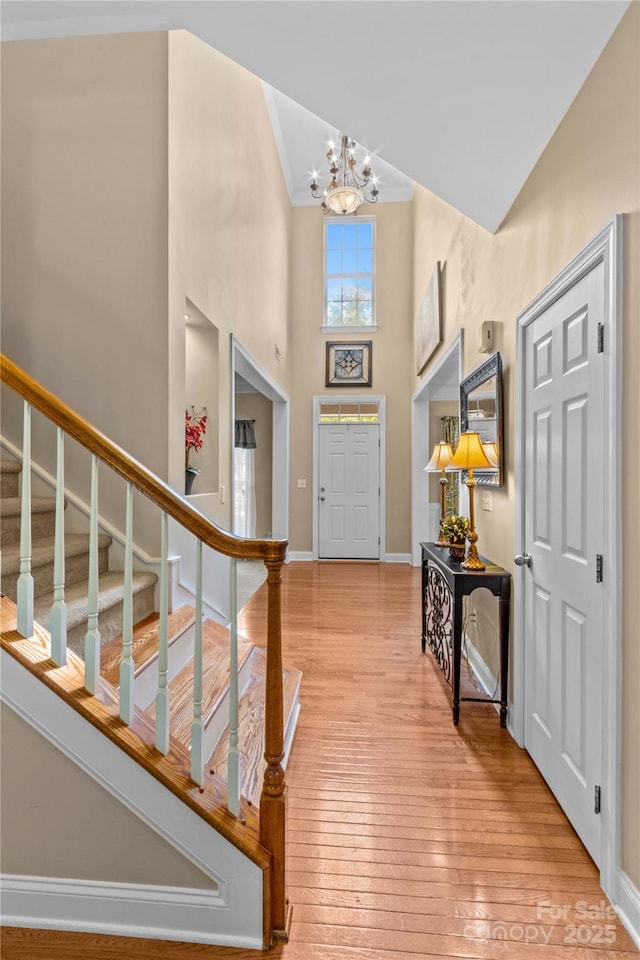 foyer entrance with stairs, a towering ceiling, baseboards, light wood finished floors, and a notable chandelier