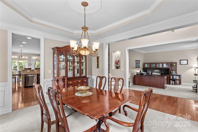 dining space with light wood-type flooring, a chandelier, crown molding, and a wainscoted wall