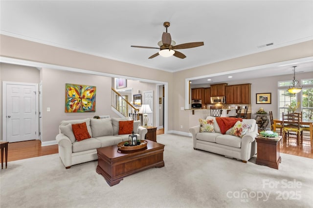 living room with stairs, visible vents, ceiling fan, crown molding, and baseboards