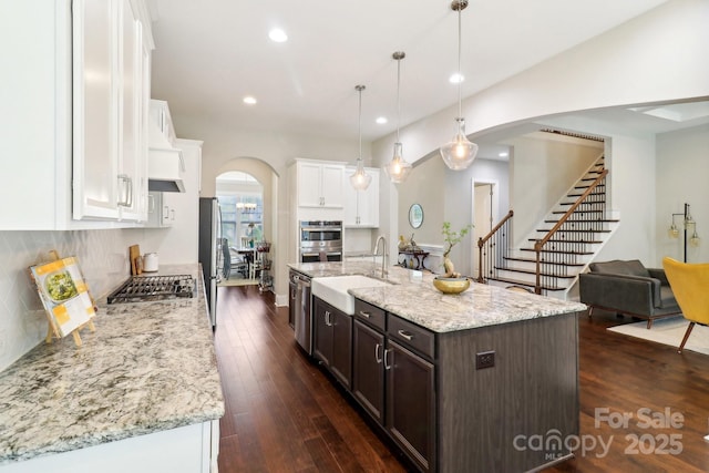 1004 Princesa Dr, Matthews, NC 28104 - kitchen with dark brown cabinetry, arched walkways, a sink, stainless steel appliances, and white cabinetry