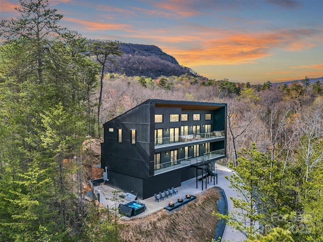 back of property at dusk with a patio, a mountain view, and a balcony