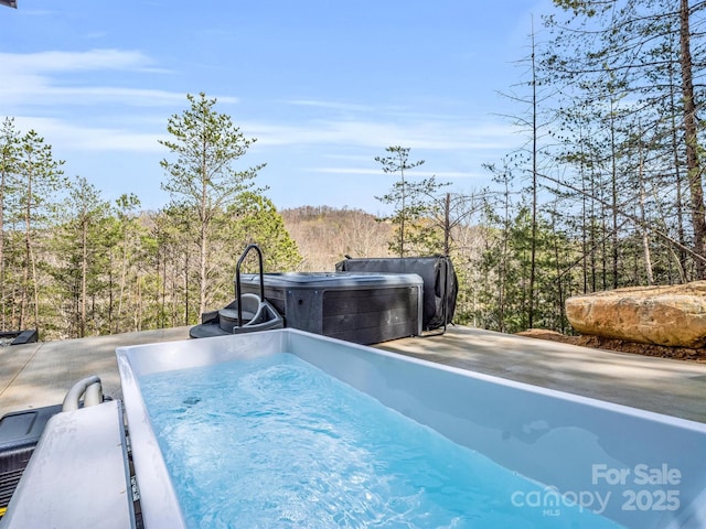view of swimming pool featuring a hot tub and a forest view
