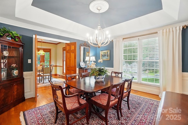 3804 Bellingham Ln, Charlotte, NC 28215 - dining room featuring a tray ceiling, a chandelier, light wood-style flooring, a wainscoted wall, and ornamental molding