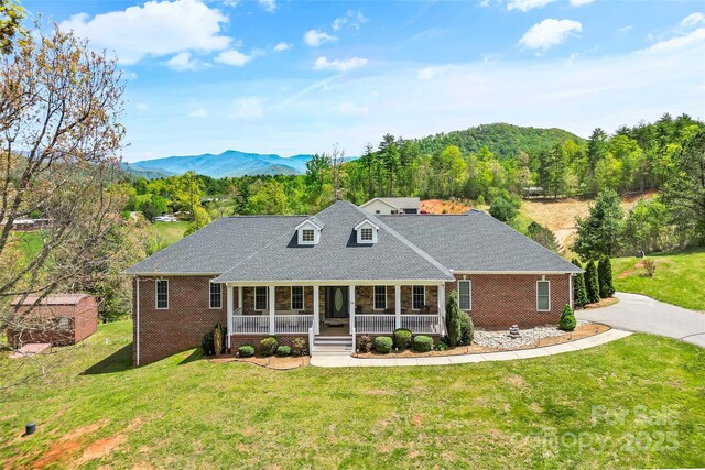 view of front of home featuring covered porch, a front yard, roof with shingles, brick siding, and a mountain view