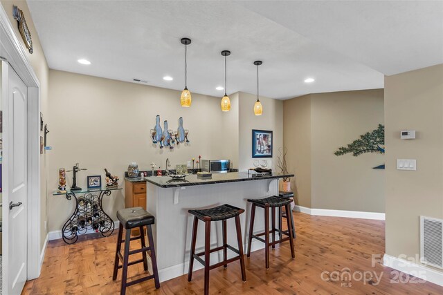 bar with baseboards, stainless steel microwave, light wood-style flooring, and visible vents