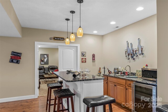 kitchen with beverage cooler, stainless steel microwave, light wood-style floors, and a kitchen bar