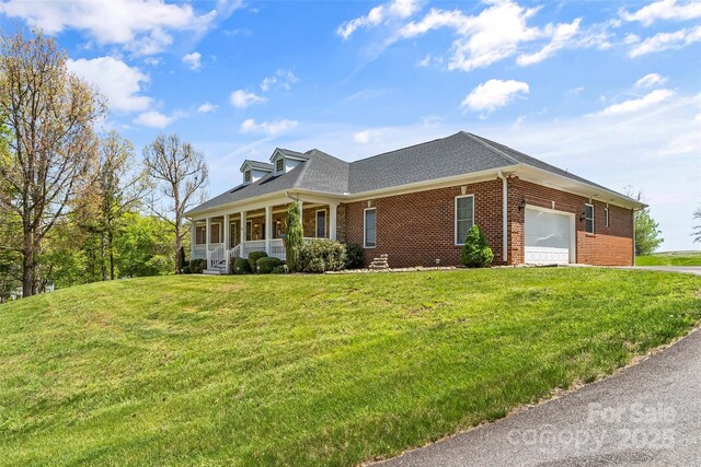 view of property exterior with a garage, covered porch, driveway, brick siding, and a yard