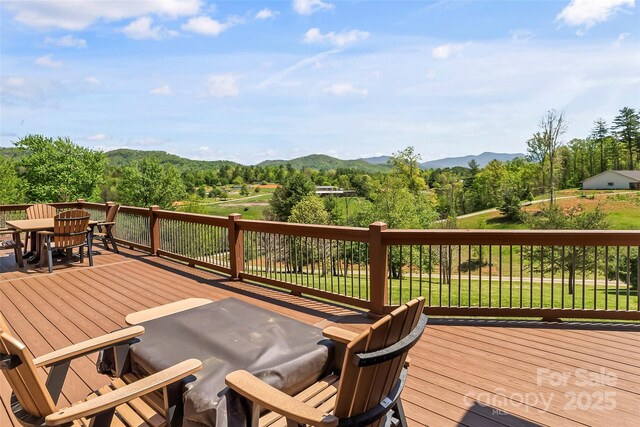 wooden terrace featuring outdoor dining space, a mountain view, and a forest view