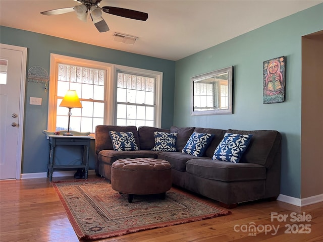 living room with hardwood / wood-style floors, visible vents, a ceiling fan, and baseboards