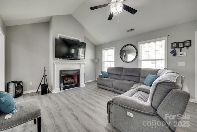 living area with wood finished floors, a fireplace, visible vents, ceiling fan, and lofted ceiling