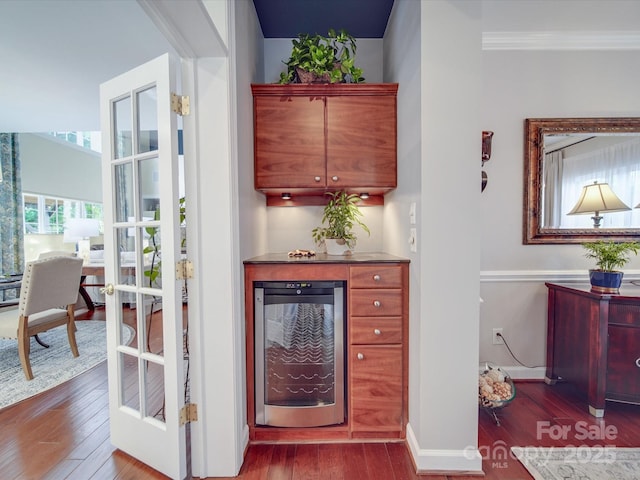 bar featuring crown molding, beverage cooler, baseboards, and dark wood finished floors