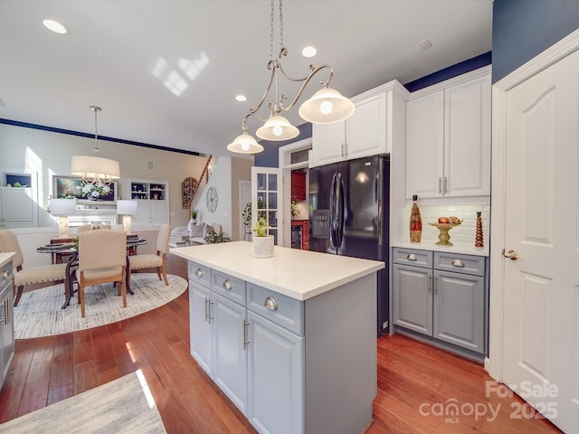kitchen with white cabinets, black fridge, gray cabinets, a kitchen island, and hardwood / wood-style flooring