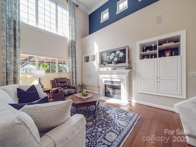 living area featuring ornamental molding, a glass covered fireplace, wood finished floors, baseboards, and a high ceiling